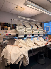 Genser i lys naturfarge beige med brodering i kontrastfarge broderes i stor broderingsmaskin med fire hoder
