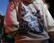 Premium tykk hoodie i naturlig beige farge med kongeblått detaljrikt design av fugler, blomster, fjell i et utopia